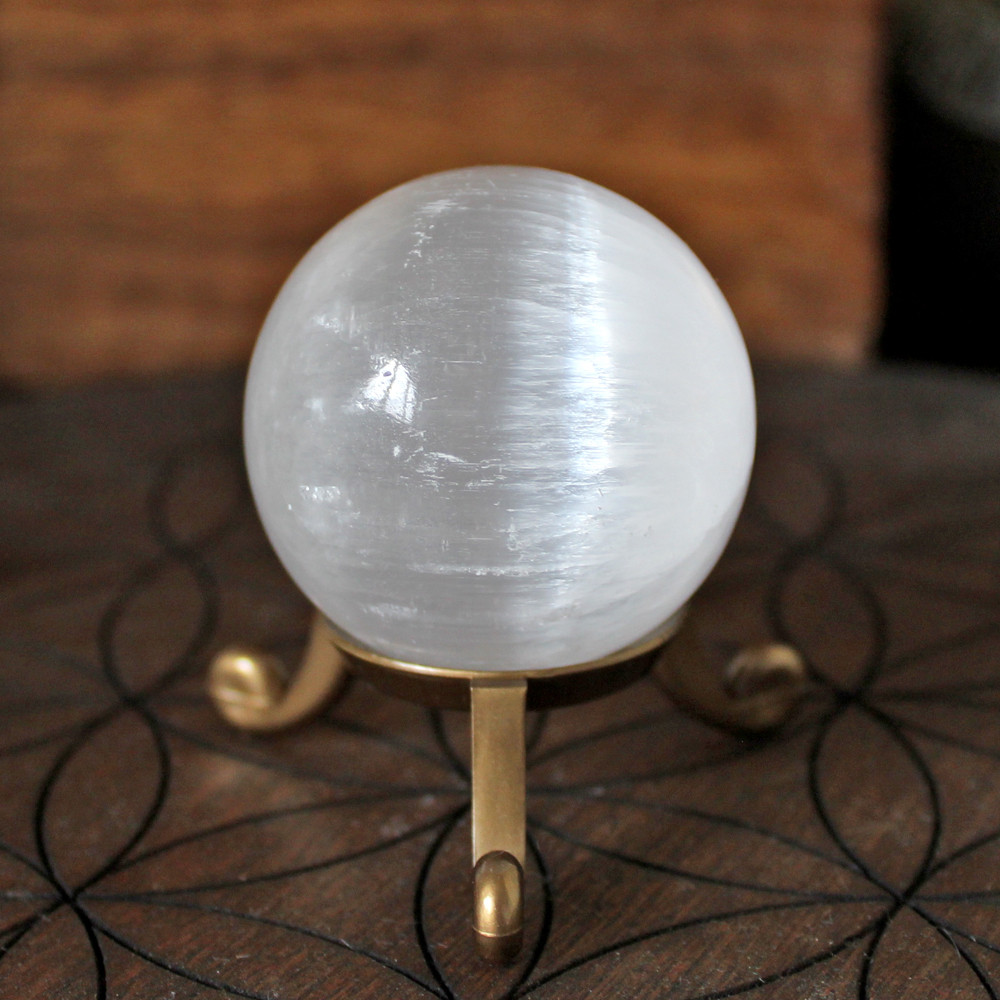 Selenite (Satin Spar) Crystal Sphere with a brass effect tripod stand on a wooden flower of life crystal grid board