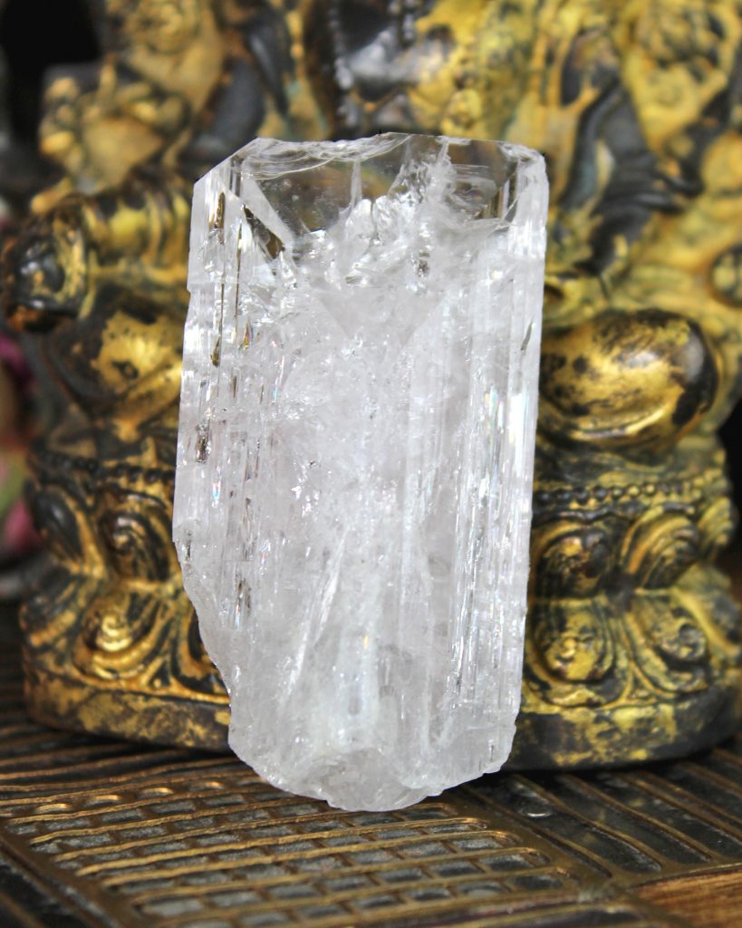 Danburite crystal leaning on a gold buddha statue